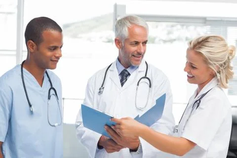 Three smiling doctors examining a file Stock Photos