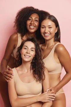 Three smiling girlfriends posing in the studio wearing a comfortable beige Stock Photos