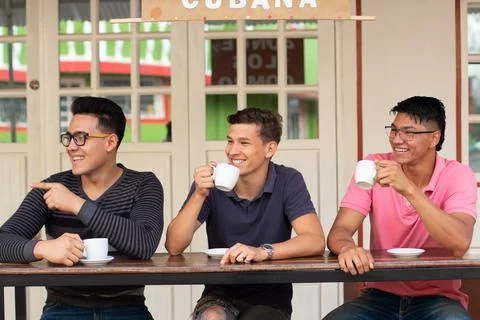 Three smiling students drinking at an outdoor latin cafe while looking Stock Photos