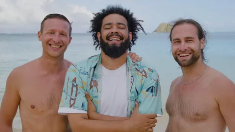 Three smiling young men posing for a picture on the beach with view on the ocean Video stock 267327175