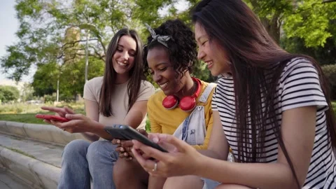 Three smiling young women using cell phone outdoors. Group of happy friends Stock Footage 245764981