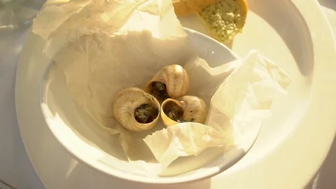 Three snails are cooked in a white plate. Then they take one of them. Cooked Stock Footage 92498882