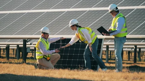 Three solar panel technicians examining a solar panel on a solar farm Video stock 144246764