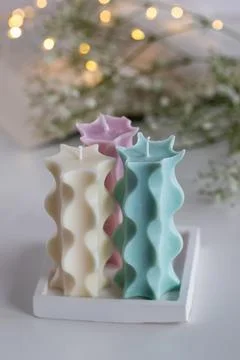 Three soy candles on table. Book, flowers and lights in background. Home deco Stock Photos