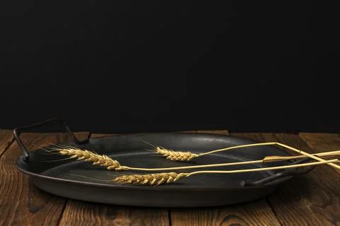 Three spikelets of ripe wheat lie on a rustic plate on an old wooden table. C Foto stock