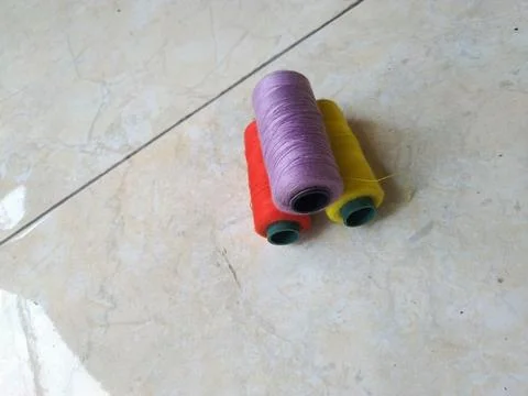Three spools of colored thread on floor background. Coils of yellow, violet and  Stock Photos
