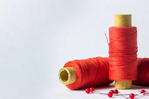 Three spools of scarlet thread. Nearby are needles with scarlet heads. Stock Photos