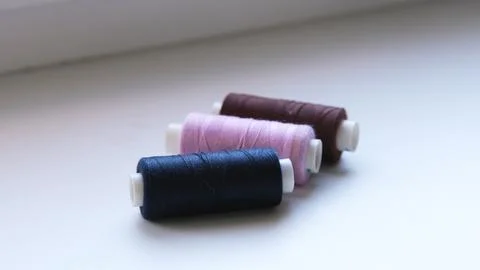 Three spools of sewing thread in dark blue, pink and brown lie in a row on a Stock Photos