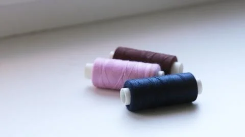 Three spools of sewing thread in dark blue, pink and brown lie in a row on a Stock Photos