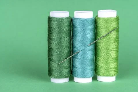 Three spools of sewing thread of different shades of green with a needle stuc Stock Photos