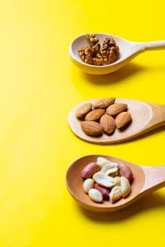 Three Spoons with hazelnuts, walnuts, almonds on yellow paper Stock Photos