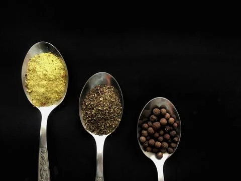 Three spoons with spices on black background Stock Photos