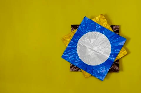 Three square pieces of colored foil on yellow. Stock Photos