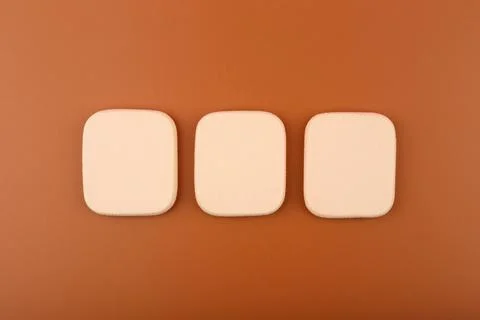 Three square shaped make up sponges on brown background Stock Photos