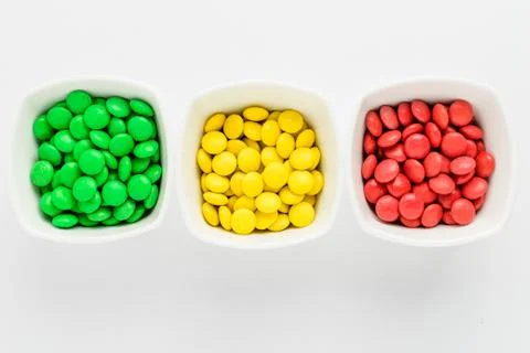 Three squared bowls with small red, yellow and green coated chocolate candies Stock Photos