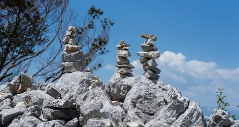 Three stacked stone cairns stand balanced on a rugged rocky peak Stock Photos