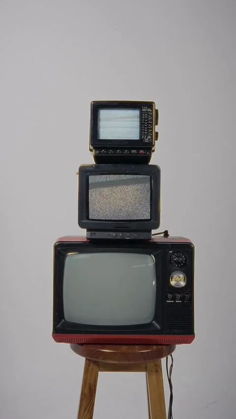 Three stacked vintage televisions displaying static on wooden stool Video stock 331773035