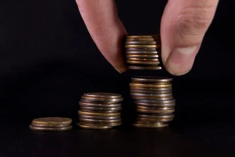 Three stacks of coins hand raised piece of coins on black leather Stock Photos