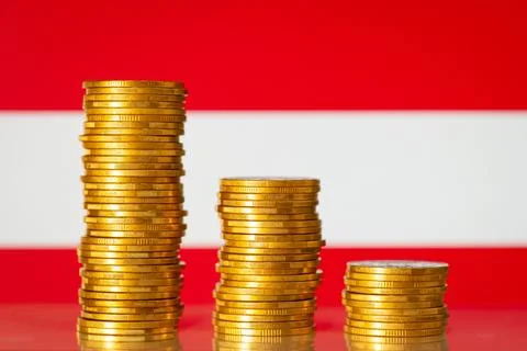 Three stacks of gold coins from highest to lowest against flag of Austria Stock Photos