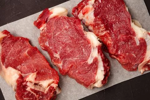 Three steaks of raw marbled beef on parchment paper, top view Stock Photos
