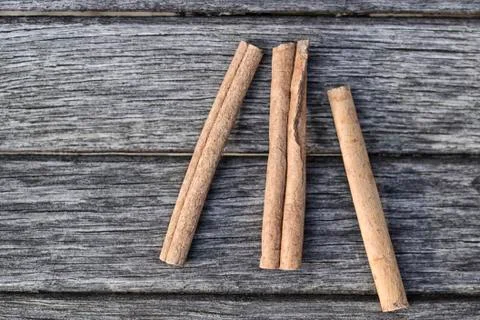 Three sticks of cinnamon lie on the background of old boards Stock Photos