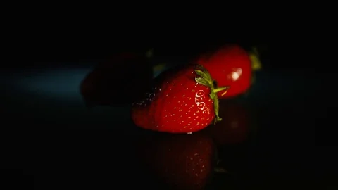 Three strawberries lie on a dark table on a black background in the light. HD Stock Footage 89763480