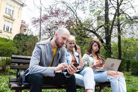 Three students on a bench in the park study talking typing on laptop notebo.. Stock Photos