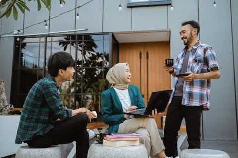 Three students chatting doing assignments in front of the building Stock Photos