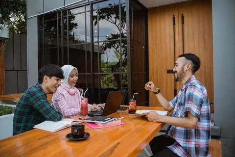 Three students chatting happily while doing assignments in a cafe Stock Photos