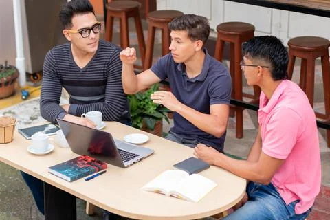 Three students chatting in an open-air latin coffee shop. latin venue concept Fotos de archivo