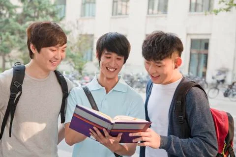 Three students discussing and looking at the book Stock Photos