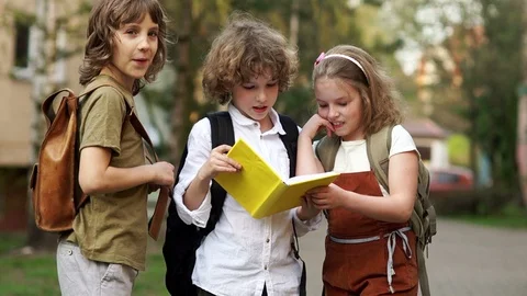 Three students look at the book and laugh gaily. The boys look slyly. Children's Stock Footage 89608335