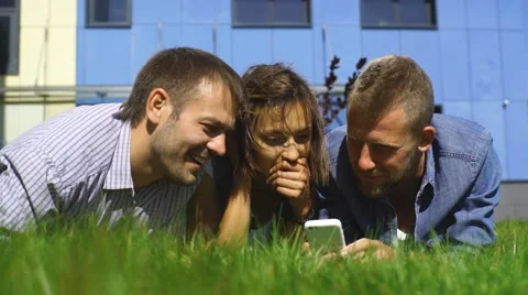 Three students lying on the lawn and use the phone Stock Footage 67833908