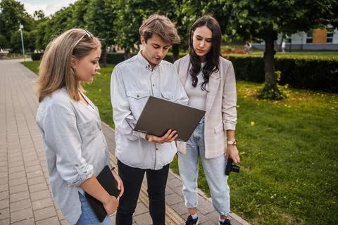 Three students in natural park browsing laptop in summertime 库存照片