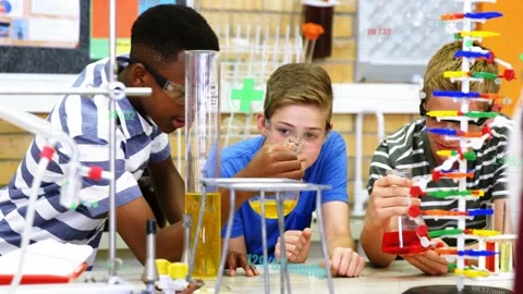 Three students at science bench, center lifting beaker, testing sample, green Stock Footage 333790369
