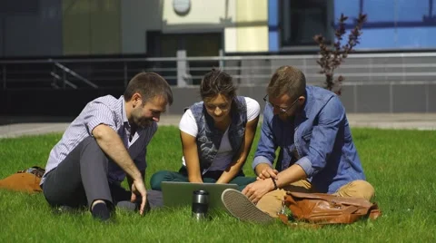 Three students sit on the lawn and prepare for lessons Stock Footage 67833289