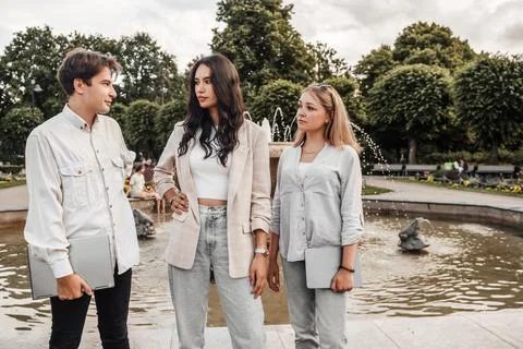 Three students talking around park fountain in summertime Stock Photos