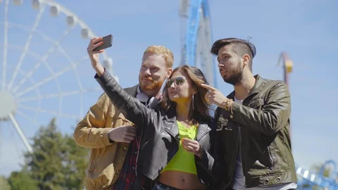 Three students wave hands while making selfies in amusement park Vidéo 116495696