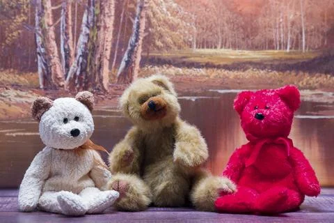 Three stuffed bears sit together on a wooden surface Stock Photos