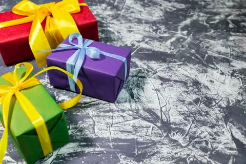 Three stylish multicolored gift boxes with bright ribbons on grey background Stock Photos