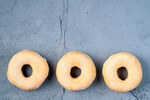 Three sugar glazed donuts lying in a row on dark background Stock Photos