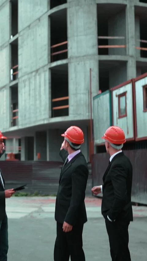 Three suited men in hard hats confidently discuss a construction site Stock Footage 305490866