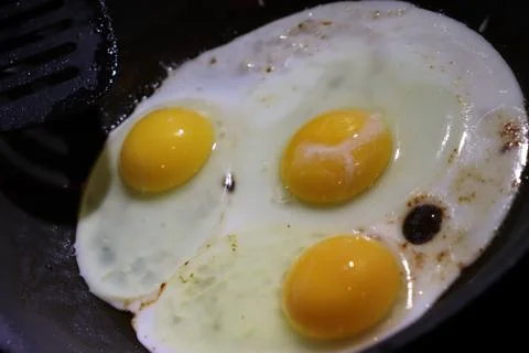 Three sunny side up eggs cooking in frying pan Stock Photos