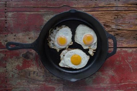 Three sunny side up fried eggs in cast iron pan flat lay Stock Photos