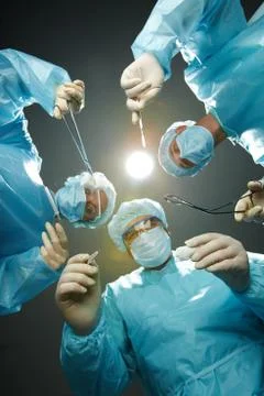 Three surgeons bending over a patient with forceps Stock Photos