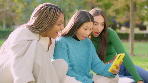 Three surprised friends using a mobile sitting outdoors Vídeo Stock 234858395