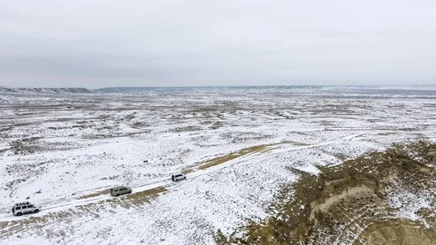 Three SUVs moving along the edge of a sandy cliff of the snow-covered desert in Stock Footage 93836402