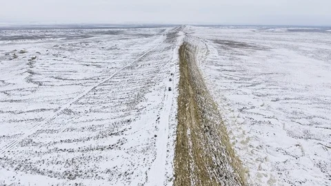 Three SUVs moving along the edge of a sandy cliff of the snow-covered desert in Stock Footage 93995130