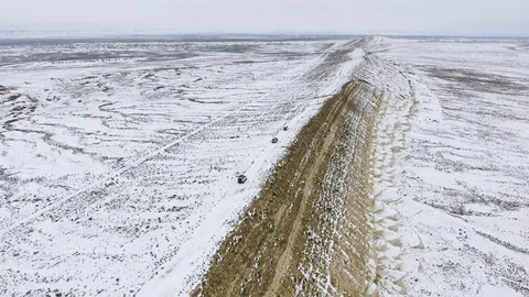 Three SUVs moving along the edge of a sandy cliff of the snow-covered desert in Stock Footage 93995494