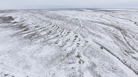 Three SUVs moving along the edge of a sandy cliff of the snow-covered desert in Stock Footage 93996595